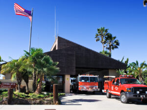 Fire station 6 has palm trees planted in the front of the American flag. Both engine 66 and ocean rescue 66 are parked in the driveway.